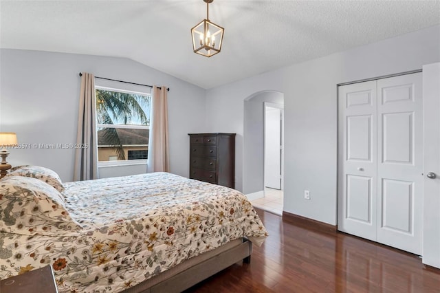 bedroom with vaulted ceiling, dark hardwood / wood-style floors, a textured ceiling, and a closet