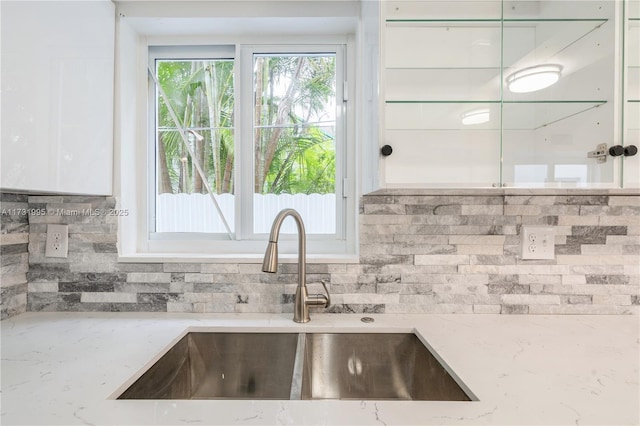 kitchen featuring tasteful backsplash, light stone countertops, sink, and white cabinets