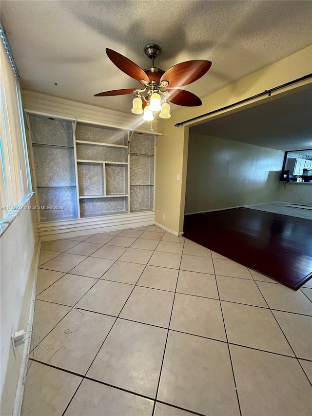 unfurnished living room featuring built in shelves, ceiling fan, a textured ceiling, and light tile patterned floors