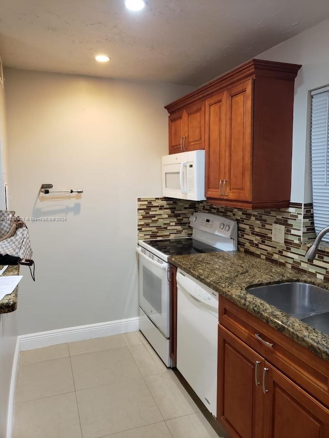 kitchen with light tile patterned flooring, sink, dark stone countertops, white appliances, and decorative backsplash