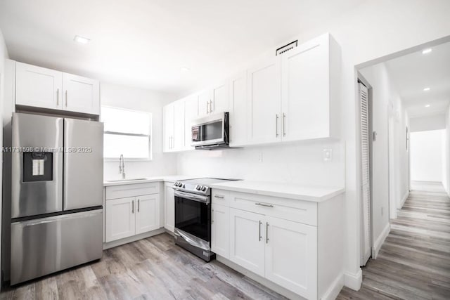 kitchen featuring sink, backsplash, white cabinets, light hardwood / wood-style floors, and stainless steel appliances