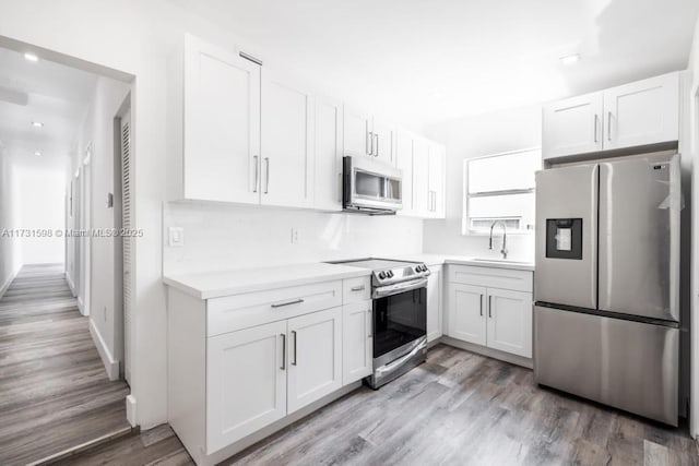 kitchen with white cabinetry, sink, stainless steel appliances, and light hardwood / wood-style floors