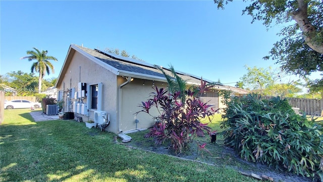 view of side of property with cooling unit, a lawn, and solar panels