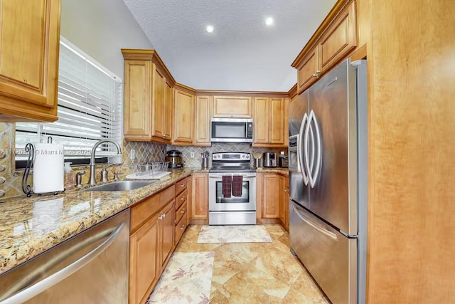 kitchen with sink, tasteful backsplash, a textured ceiling, appliances with stainless steel finishes, and light stone countertops