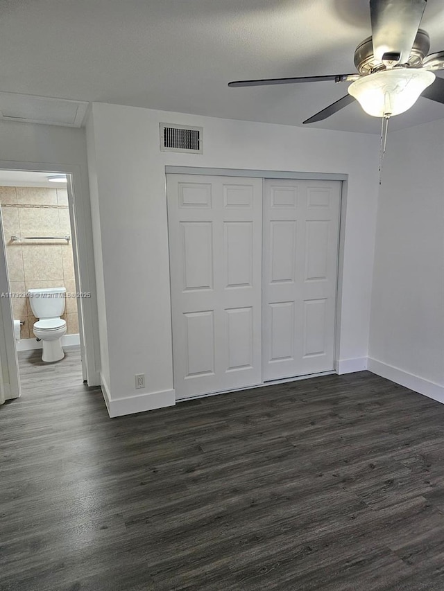 unfurnished bedroom featuring ensuite bath, dark wood-type flooring, ceiling fan, and a closet