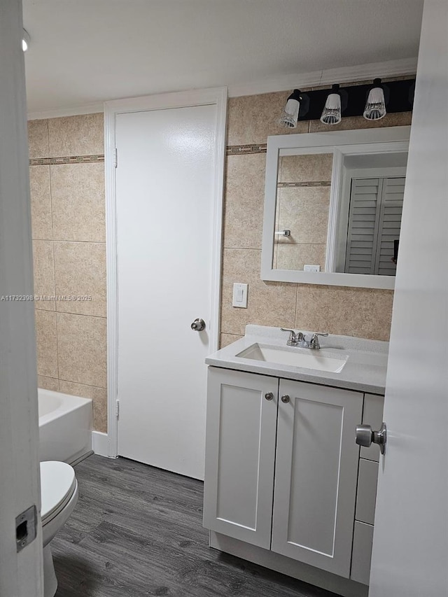 bathroom with wood-type flooring, tile walls, vanity, and toilet