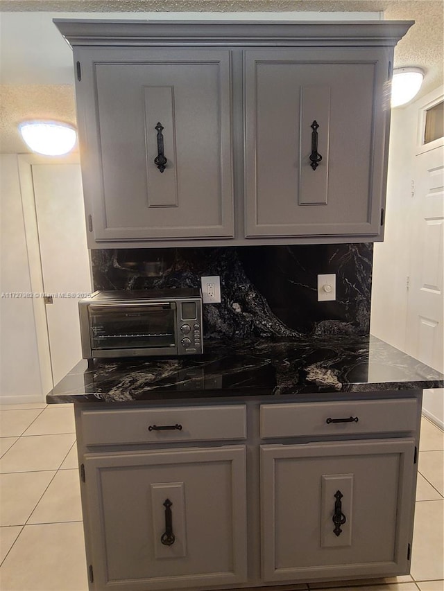 kitchen featuring tasteful backsplash, gray cabinets, light tile patterned floors, and dark stone countertops