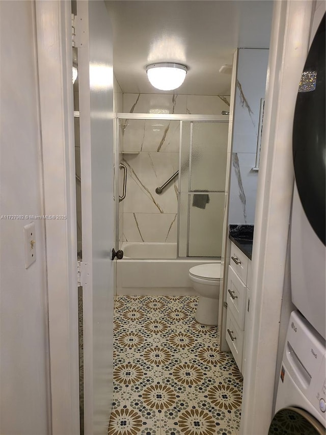 full bathroom featuring toilet, stacked washer / dryer, shower / bath combination with glass door, and vanity