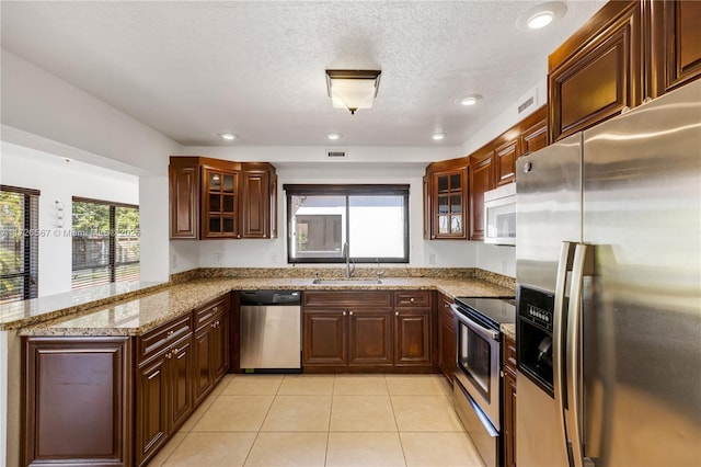 kitchen featuring appliances with stainless steel finishes, sink, light tile patterned floors, kitchen peninsula, and light stone countertops