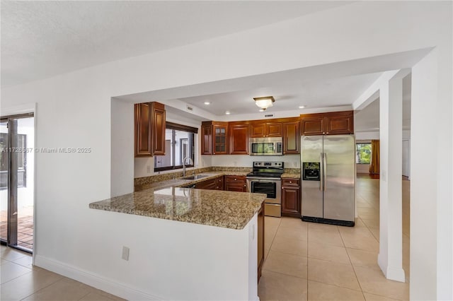 kitchen featuring sink, light tile patterned floors, kitchen peninsula, stainless steel appliances, and light stone countertops