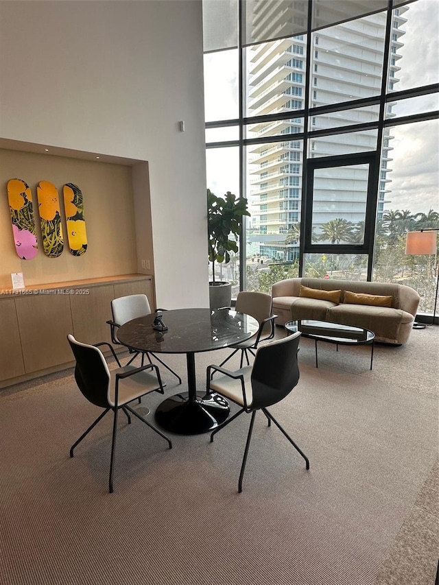 carpeted dining room with plenty of natural light, floor to ceiling windows, and a high ceiling