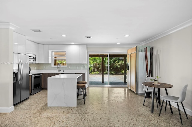 kitchen with sink, appliances with stainless steel finishes, a kitchen breakfast bar, white cabinets, and a kitchen island