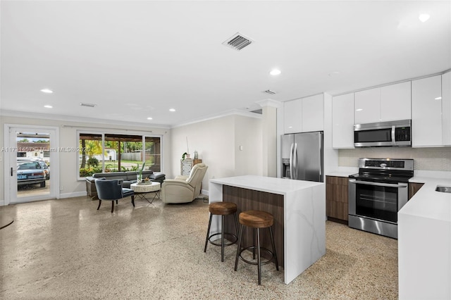 kitchen featuring crown molding, a breakfast bar area, appliances with stainless steel finishes, white cabinetry, and a center island