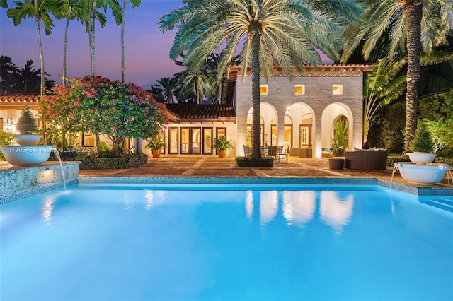 pool at dusk featuring pool water feature and a patio area