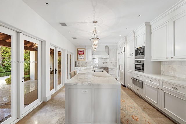 kitchen with pendant lighting, paneled fridge, an island with sink, white cabinets, and oven