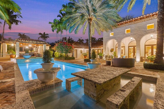 pool at dusk featuring pool water feature