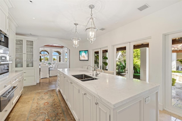 kitchen featuring french doors, sink, white cabinetry, an island with sink, and pendant lighting