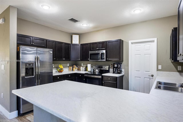 kitchen with appliances with stainless steel finishes, sink, light wood-type flooring, and kitchen peninsula