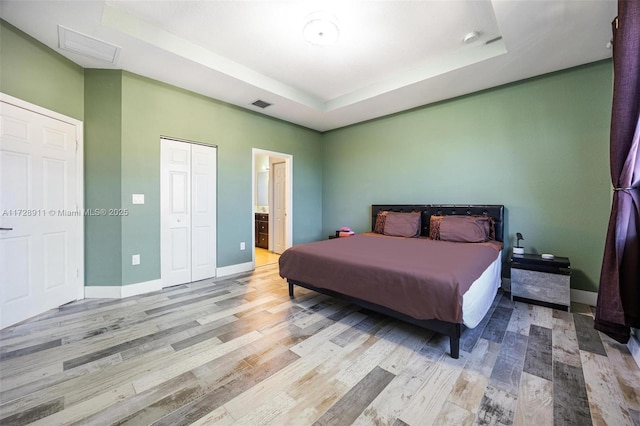 bedroom featuring ensuite bath, a raised ceiling, and light hardwood / wood-style floors