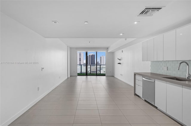 kitchen featuring light tile patterned flooring, tasteful backsplash, white cabinetry, dishwasher, and sink