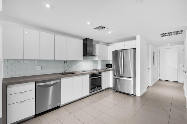 kitchen featuring light tile patterned flooring, appliances with stainless steel finishes, white cabinetry, sink, and wall chimney range hood