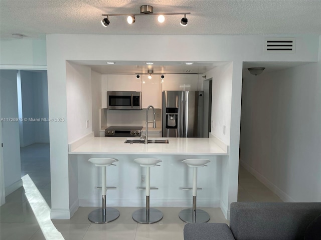 kitchen featuring a breakfast bar area, stainless steel appliances, white cabinets, a sink, and a peninsula