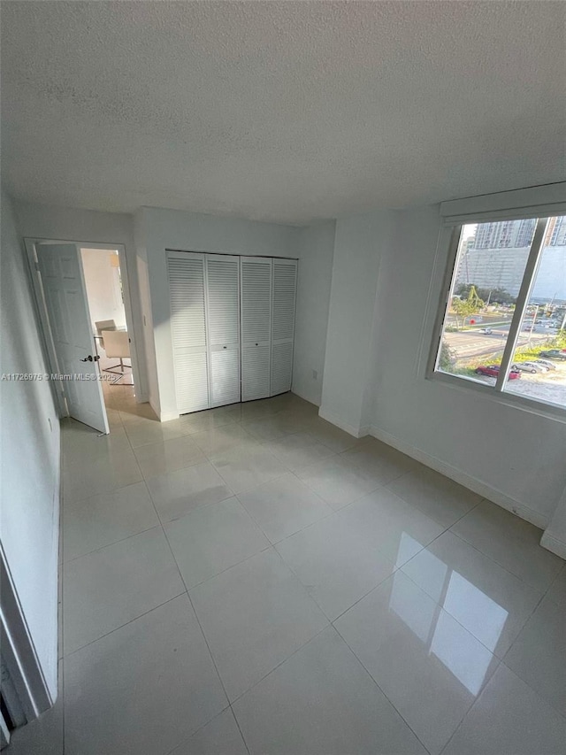 unfurnished bedroom with a closet, a textured ceiling, baseboards, and light tile patterned floors