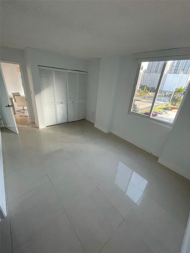 unfurnished bedroom with a closet, light tile patterned flooring, a textured ceiling, and baseboards