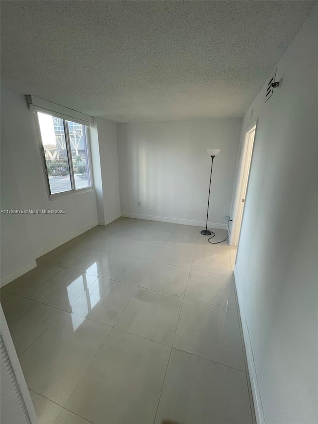 empty room with a textured ceiling, light tile patterned flooring, and baseboards