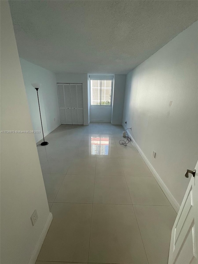 unfurnished bedroom featuring light tile patterned floors, baseboards, and a textured ceiling