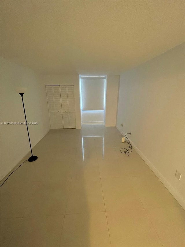 spare room featuring light tile patterned floors, baseboards, and a textured ceiling