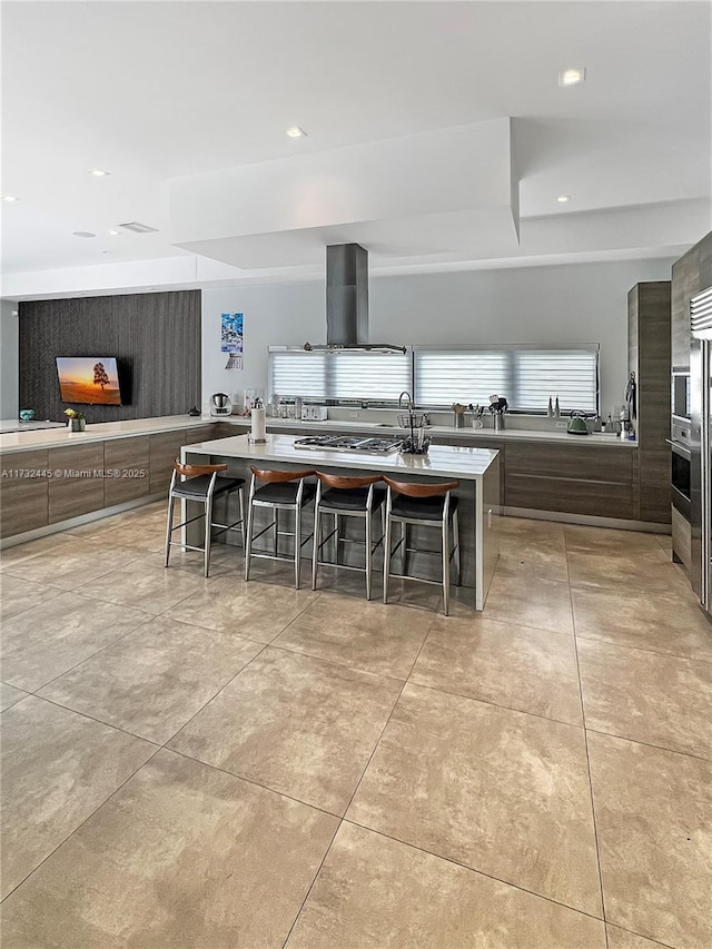 kitchen with appliances with stainless steel finishes, an island with sink, a breakfast bar area, island exhaust hood, and light tile patterned floors