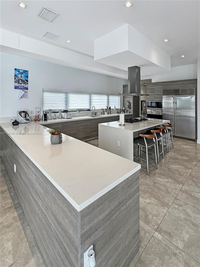 kitchen with a spacious island, a kitchen bar, built in appliances, kitchen peninsula, and island exhaust hood