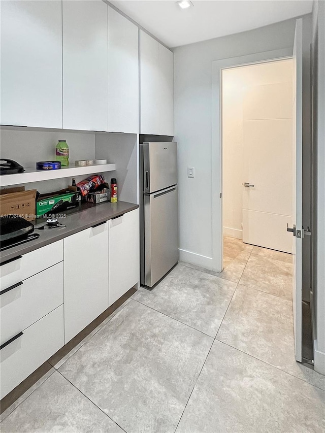 kitchen featuring light tile patterned floors, stainless steel fridge, and white cabinets