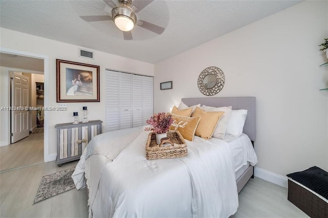 bedroom featuring light wood-type flooring, a textured ceiling, ceiling fan, and a closet