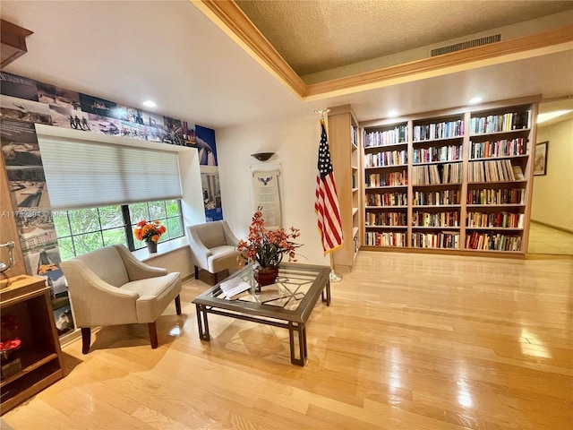 sitting room with a raised ceiling, crown molding, and light hardwood / wood-style flooring