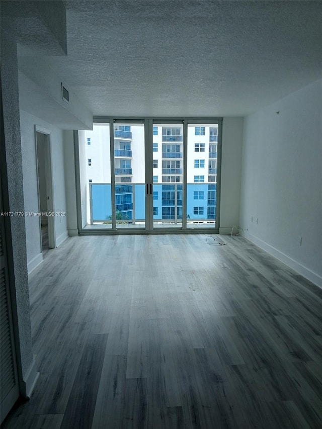 spare room with expansive windows, wood-type flooring, and a textured ceiling