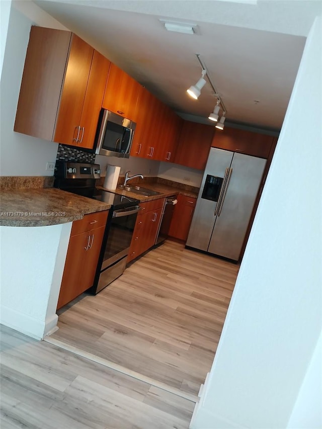 kitchen featuring appliances with stainless steel finishes, rail lighting, sink, decorative backsplash, and light hardwood / wood-style flooring