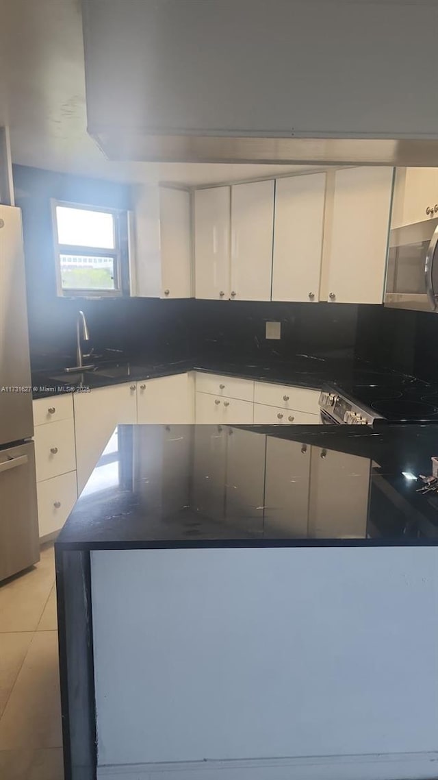 kitchen with white cabinetry, sink, light tile patterned floors, and stainless steel fridge