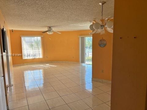 tiled empty room featuring ceiling fan with notable chandelier and a textured ceiling