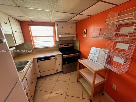 kitchen with white cabinetry, light tile patterned floors, dishwasher, stainless steel electric stove, and a drop ceiling