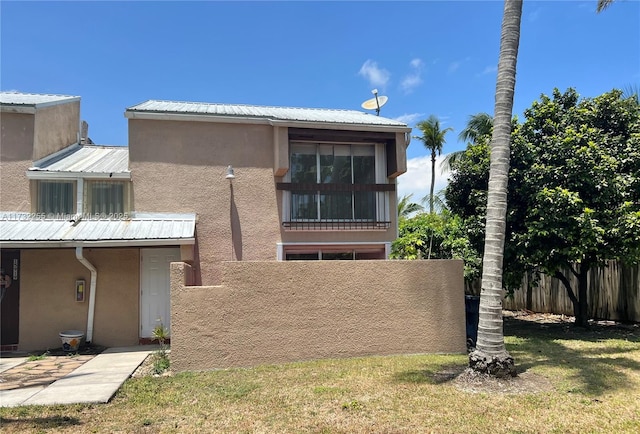 view of front facade with metal roof, stucco siding, a front yard, and fence