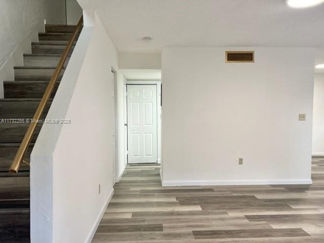 empty room featuring visible vents, wood finished floors, baseboards, and stairway