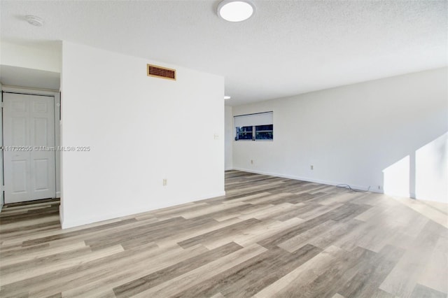 spare room with light wood-style floors, visible vents, baseboards, and a textured ceiling
