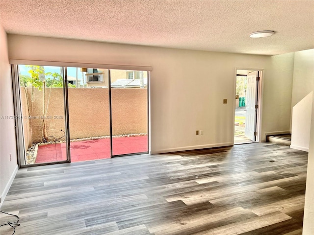unfurnished room featuring a textured ceiling, baseboards, and wood finished floors