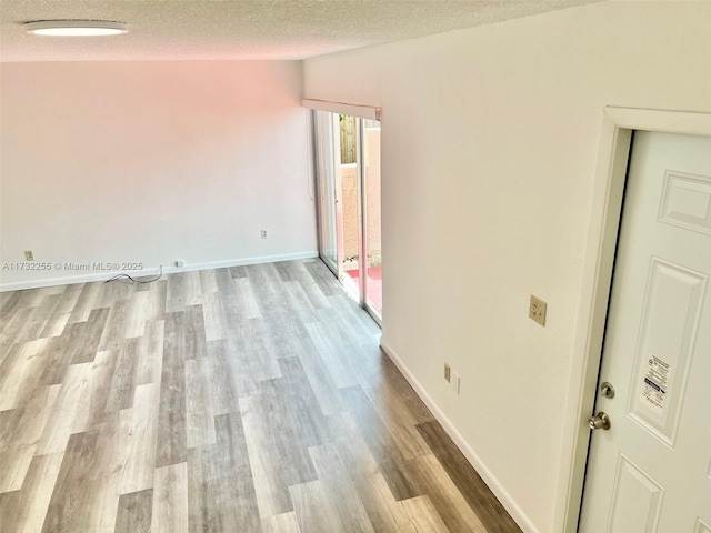 empty room with baseboards, a textured ceiling, and wood finished floors