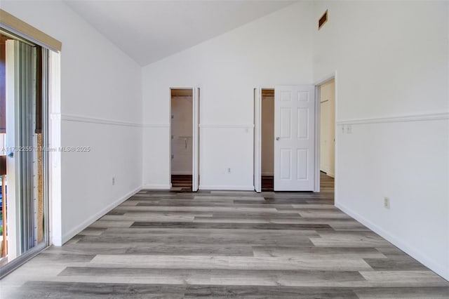 unfurnished bedroom with baseboards, high vaulted ceiling, visible vents, and wood finished floors