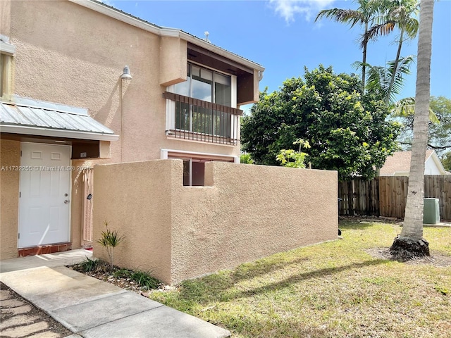 view of property exterior with a yard, stucco siding, fence, and metal roof