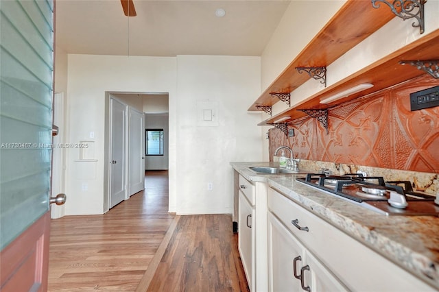 kitchen with sink, white cabinetry, light stone counters, stainless steel gas stovetop, and light hardwood / wood-style floors