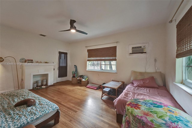 bedroom featuring hardwood / wood-style flooring, a wall unit AC, and ceiling fan